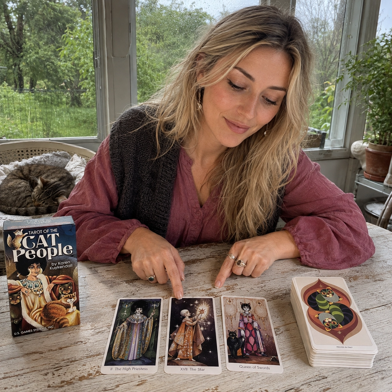 Aurica reading Cat People Tarot with the High Priestess, Star, and Queen of Swords beside its box and stacked deck
