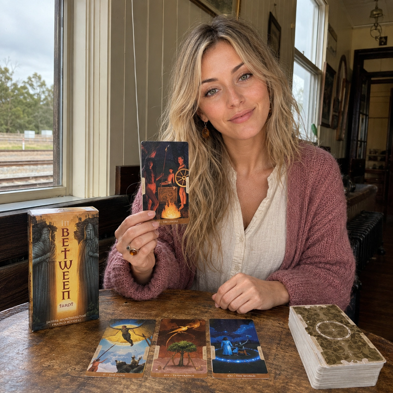 Aurica presenting The Lovers from In Between Tarot beside its box, a three-card spread, and the stacked deck