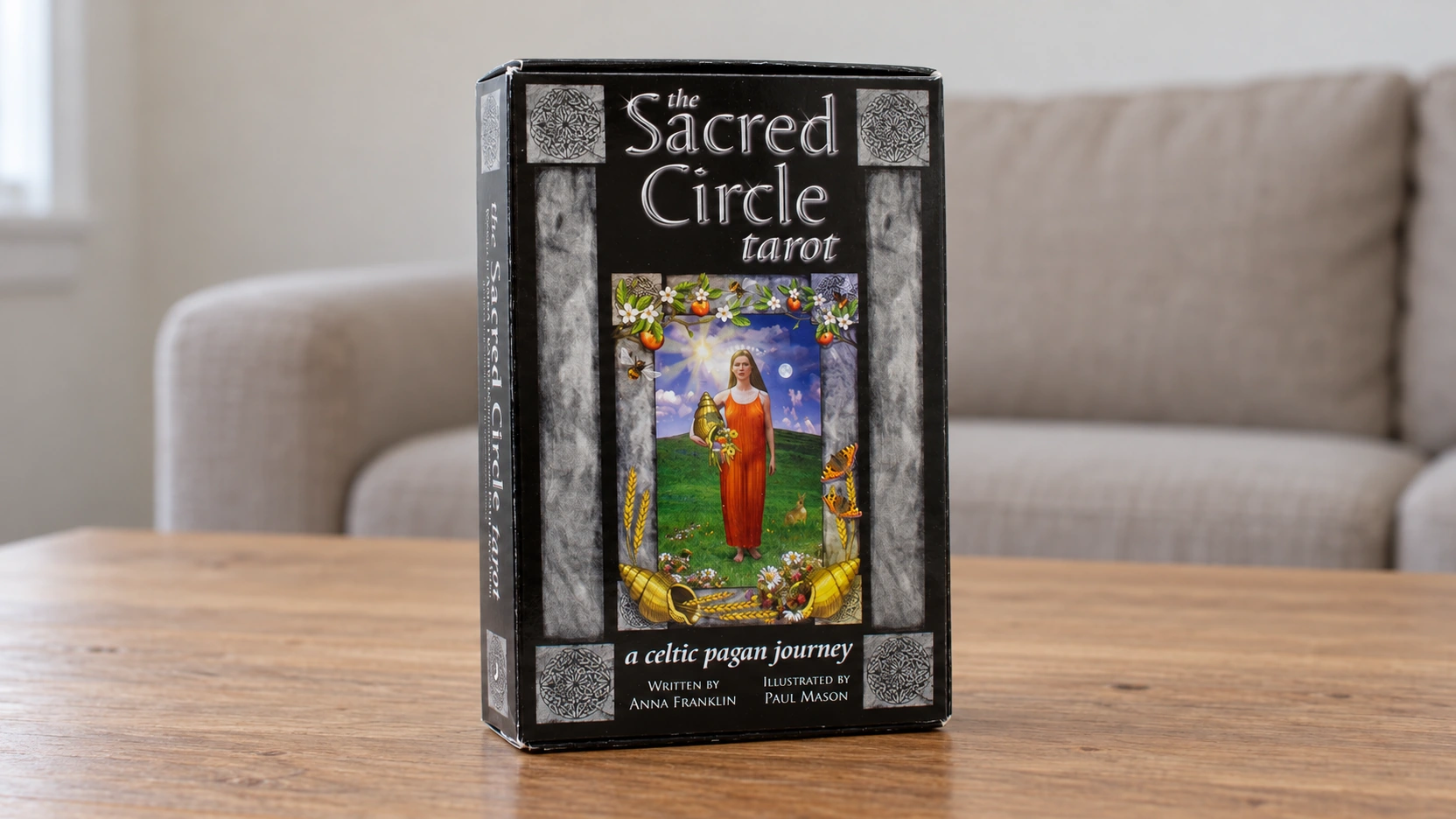 Generated scene of the supplied black Sacred Circle Tarot box, with silver title and Celtic stone framing, alone on a plain wooden table in a basic room